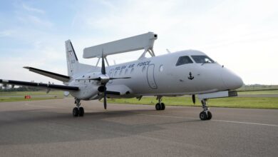 Poland's Saab 340 Airborne Early Warning (AEW) aircraft is seen on a runway. The plane is white and has "POLISH AIR FORCE" painted on its right side. Its rectangular radar system is propped up above and perpendicular to its body. Its tail number, 3401, is seen on the right side of its tail.