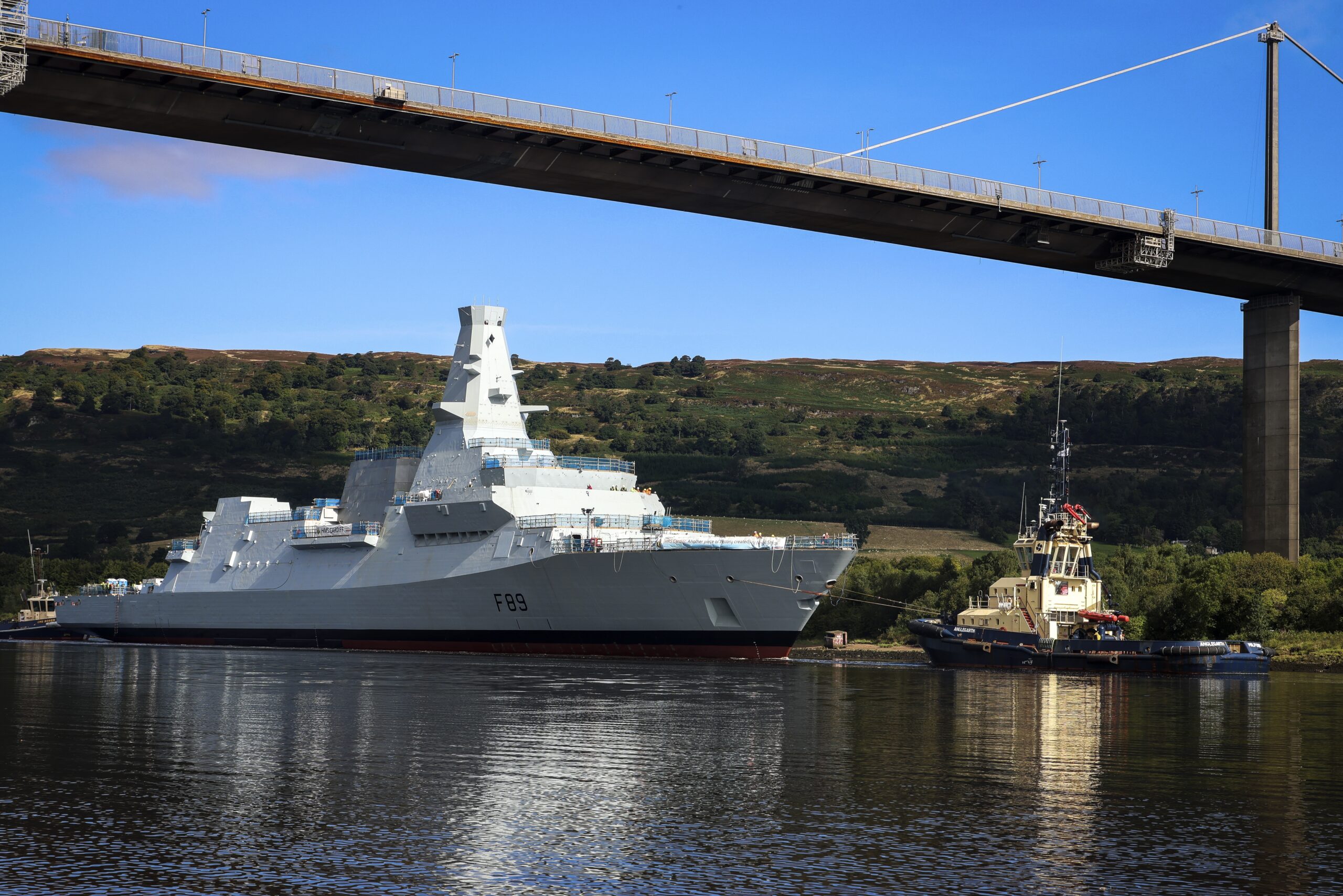 Pictured: Type 26 Frigate HMS Cardiff being towed and maneuvered as she passes under the Erskine Bridge on the Clyde.HMS Cardiff, the second of the Royal Navys new City Class Type 26 frigates, was loaded onto a giant barge last week. The ship, which weighs almost 7,000 tonnes, sailed down the River Clyde on Friday, August 30 to Loch Long, where she was lowered into the water for the first time at Glen Mallan. HMS Cardiff then made her way back up the Clyde to BAE Systems yard at Scotstoun where the work to fit the warship out will be completed. Currently Scottish shipyards have orders to build 13 Royal Navy frigates, with the Type 31 vessels being built by Babcock at Rosyth on the east coast, and the Type 26 ships being constructed by BAE Systems on the Clyde.