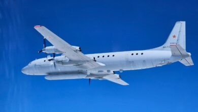 A gray Russian Il-20 aircraft, with tail ID RF-93611, is seen flying in clear blue skies. The image is taken a little below the left side of the aircraft. The Il-20 has two propellers attached on each of its wings.