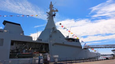 Al Emarat, the UAE Navy's second Gowind-class corvette, is seen docked at a pier. The ship is decorated with colors and flags attached to a banner hoisted up the ship's mast.