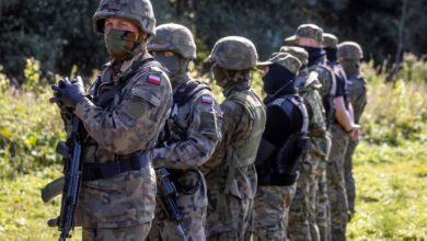 Armed Polish border guards stand next to a group of migrants on the border with Belarus